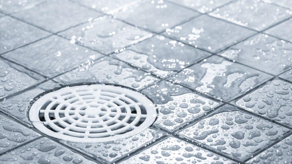 Close-up of a wet tiled floor with water droplets and a white circular drain cover.
