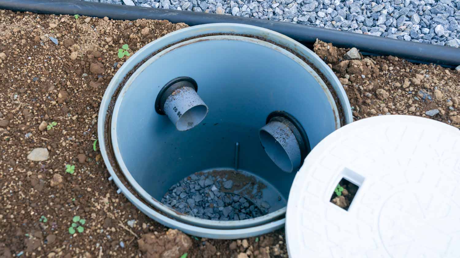 A plastic inspection chamber with two inlet pipes is installed in the ground; the cover is placed nearby on the soil.
