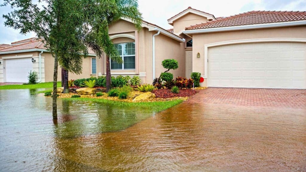 solutions for heavy rainfall Floodwater covers the driveway and front yard of a beige suburban house with a tiled roof and landscaped garden.